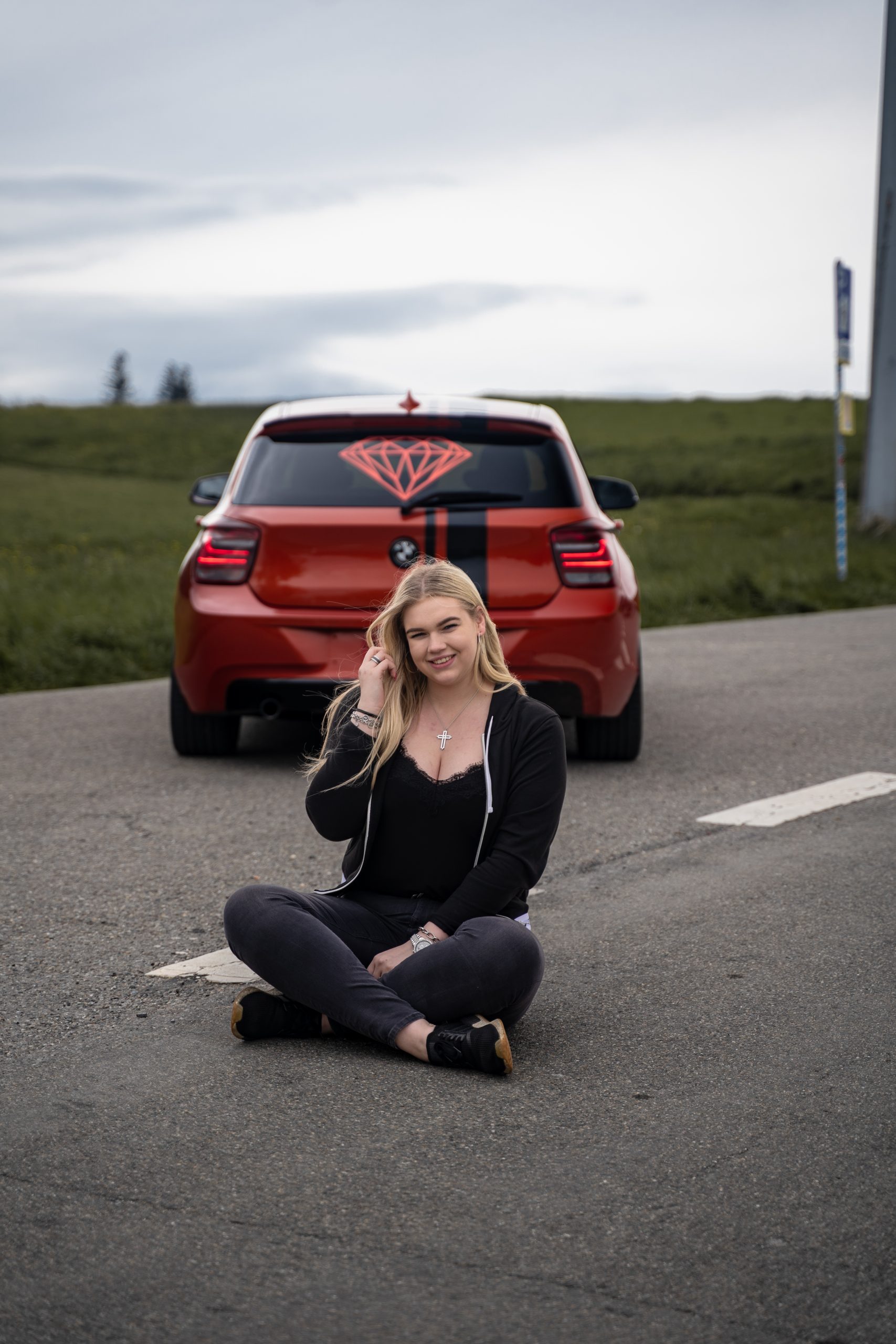 Eine blonde Frau vor einem orangenen Bmw 1er sitzend